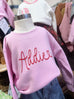 Pink sweatshirt with 'Addie' printed on it on a mannequin, surrounded by other clothing items.