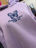 lilac colored hoodie on mannequin with blue butterfly print and words made new in cursive underneath, 2 COR. 5:17 under that. hoodie is shown on a mannequin with a mirror and other things blurred in the background