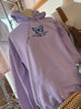 lilac colored hoodie with butterfly print and words made new in cursive writing underneath, 2 COR. 5:17 in print under that. other mannequins surrounding in background as well as a few purses and decor items